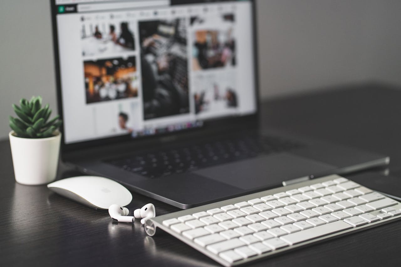 A sleek modern workspace featuring a laptop, keyboard, mouse, AirPods, and a small plant.